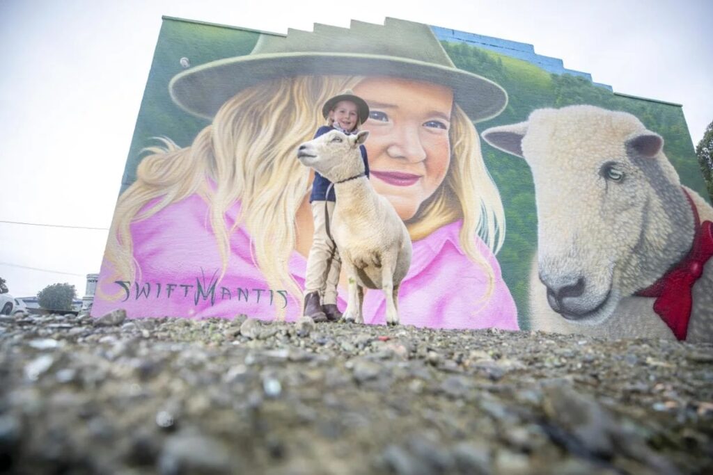 Charlee Hazlett and lamb, Ellavetta in front of the mural in Winton.